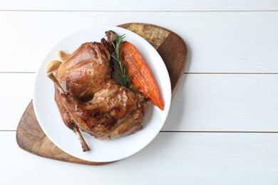 Photo of Tasty cooked rabbit meat with rosemary, garlic and carrot on white wooden table, top view. Space for text