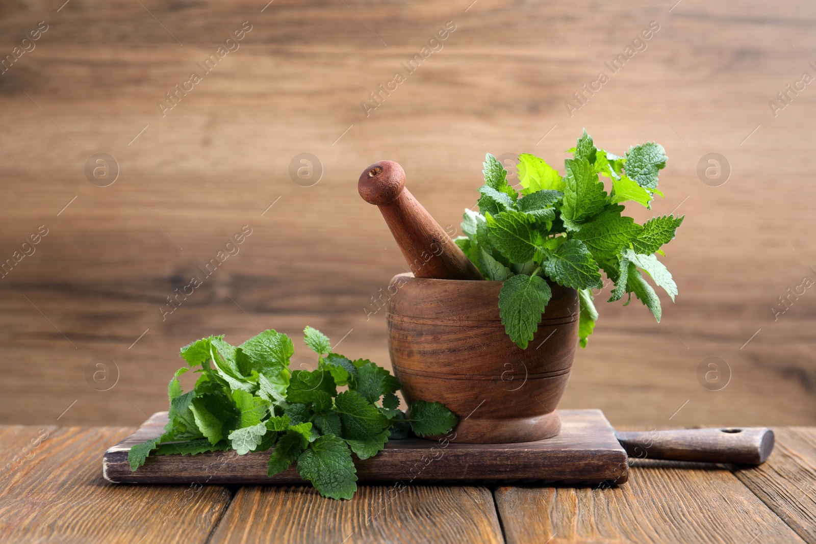 Photo of Mortar with pestle and fresh lemon balm on wooden table