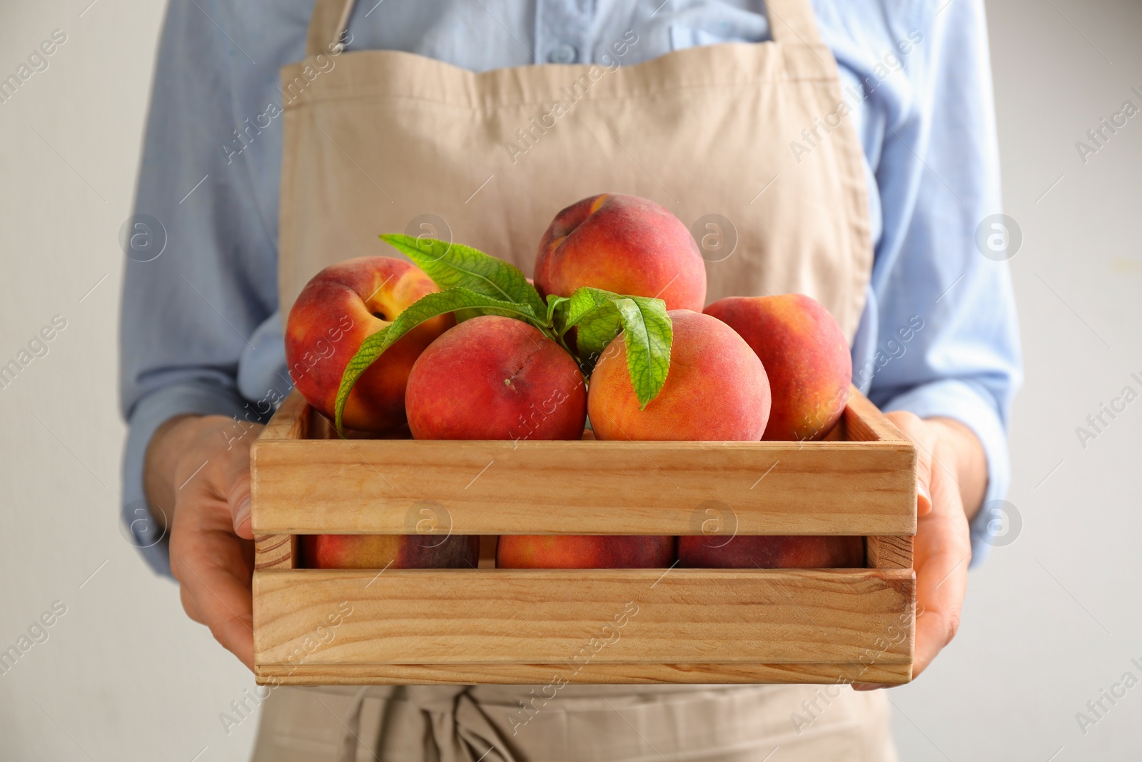 Photo of Woman with fresh sweet peaches in wooden crate, closeup