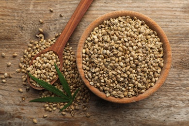 Photo of Organic hemp seeds and leaf on wooden background, flat lay