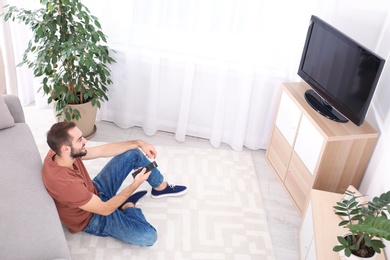 Photo of Handsome young man sitting on floor and watching TV at home
