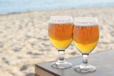 Photo of Glasses of cold beer on table near sea, space for text