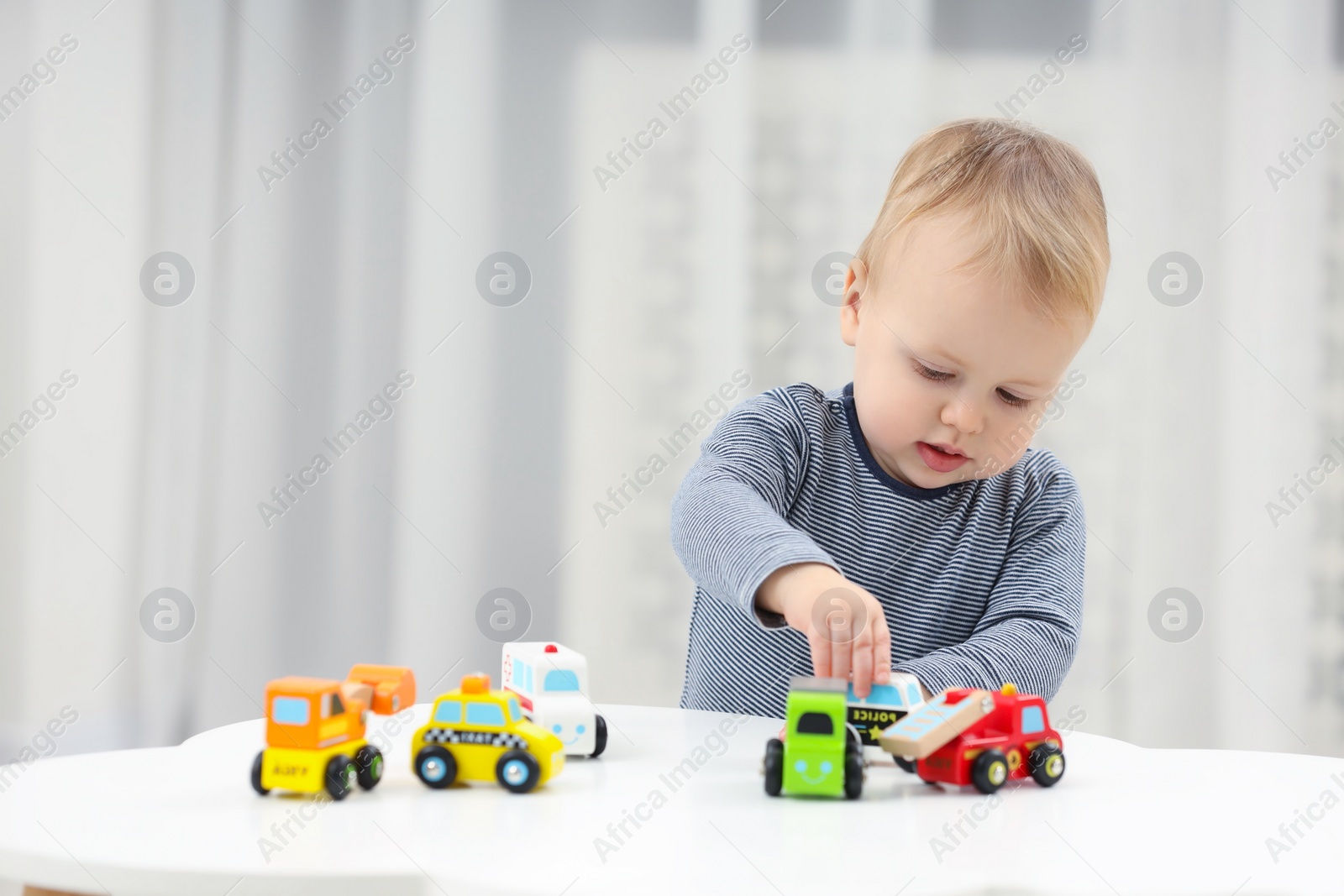 Photo of Children toys. Cute little boy playing with toy cars at white table in room, space for text