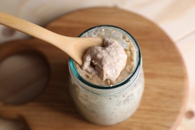 Photo of Taking sourdough starter with spoon at table, closeup