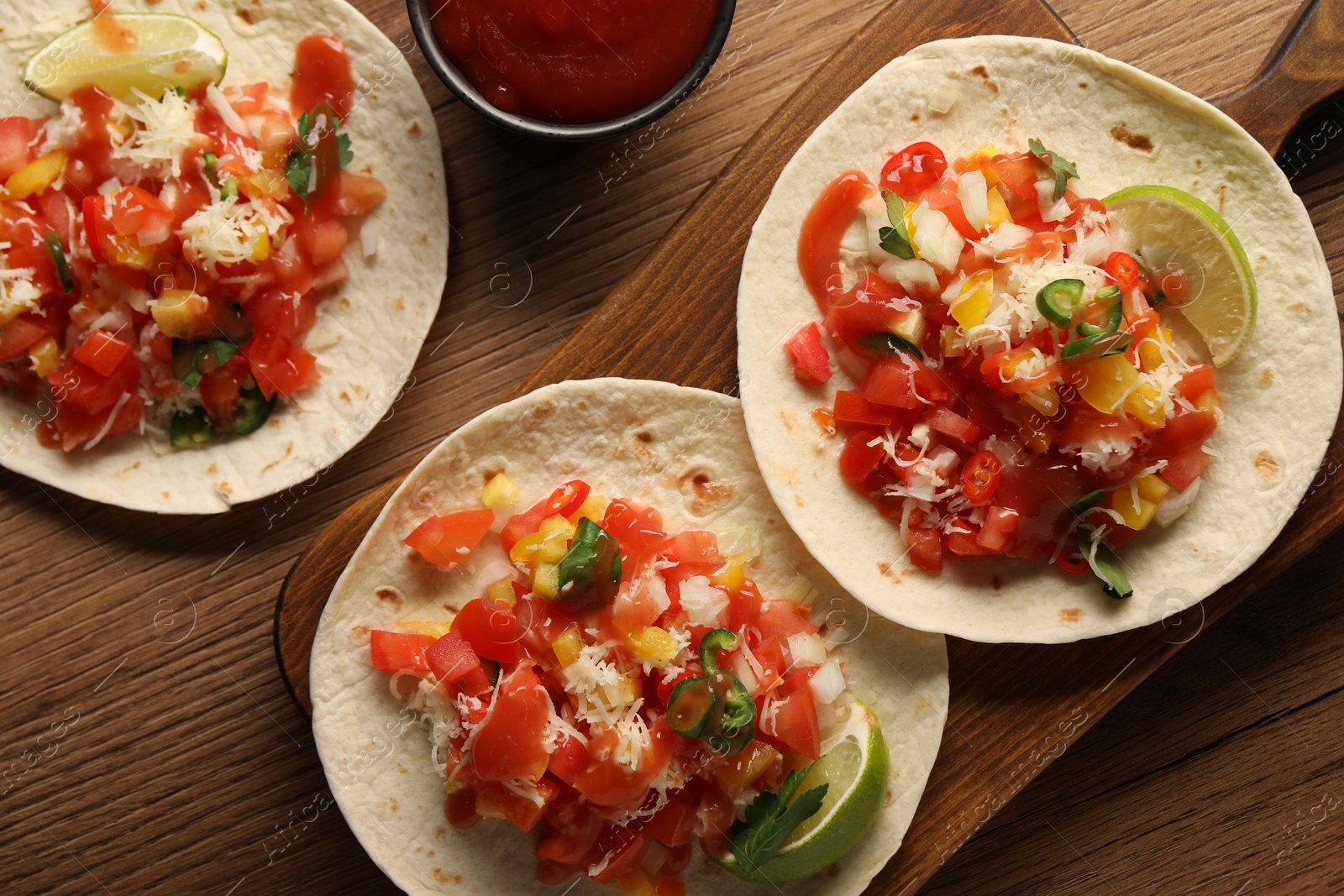 Photo of Delicious tacos with vegetables, lime and ketchup on wooden table, flat lay