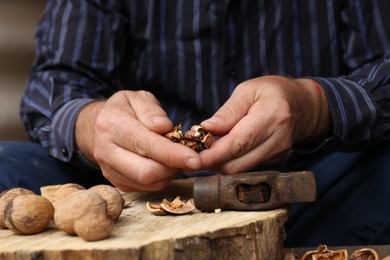 Photo of Man cracking walnuts with hammer at table, closeup