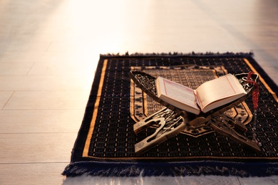 Photo of Rehal with open Quran and Muslim prayer beads on rug indoors. Space for text