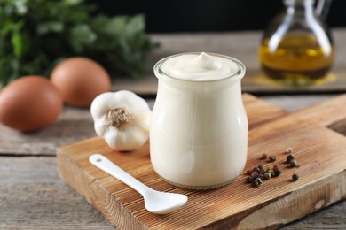 Fresh mayonnaise sauce in glass jar and ingredients on wooden table, closeup