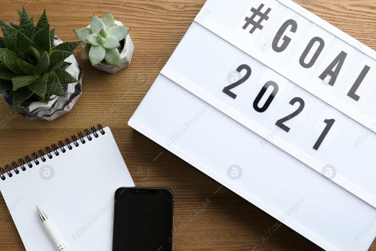 Photo of Light box with hashtag Goal 2021 near notebook, new year targets. Flat lay composition on wooden table