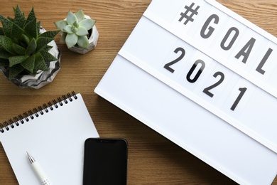 Photo of Light box with hashtag Goal 2021 near notebook, new year targets. Flat lay composition on wooden table