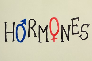 Photo of Word HORMONES drawn on beige paper sheet, top view