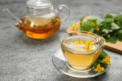 Photo of Aromatic celandine tea and flowers on grey table, space for text