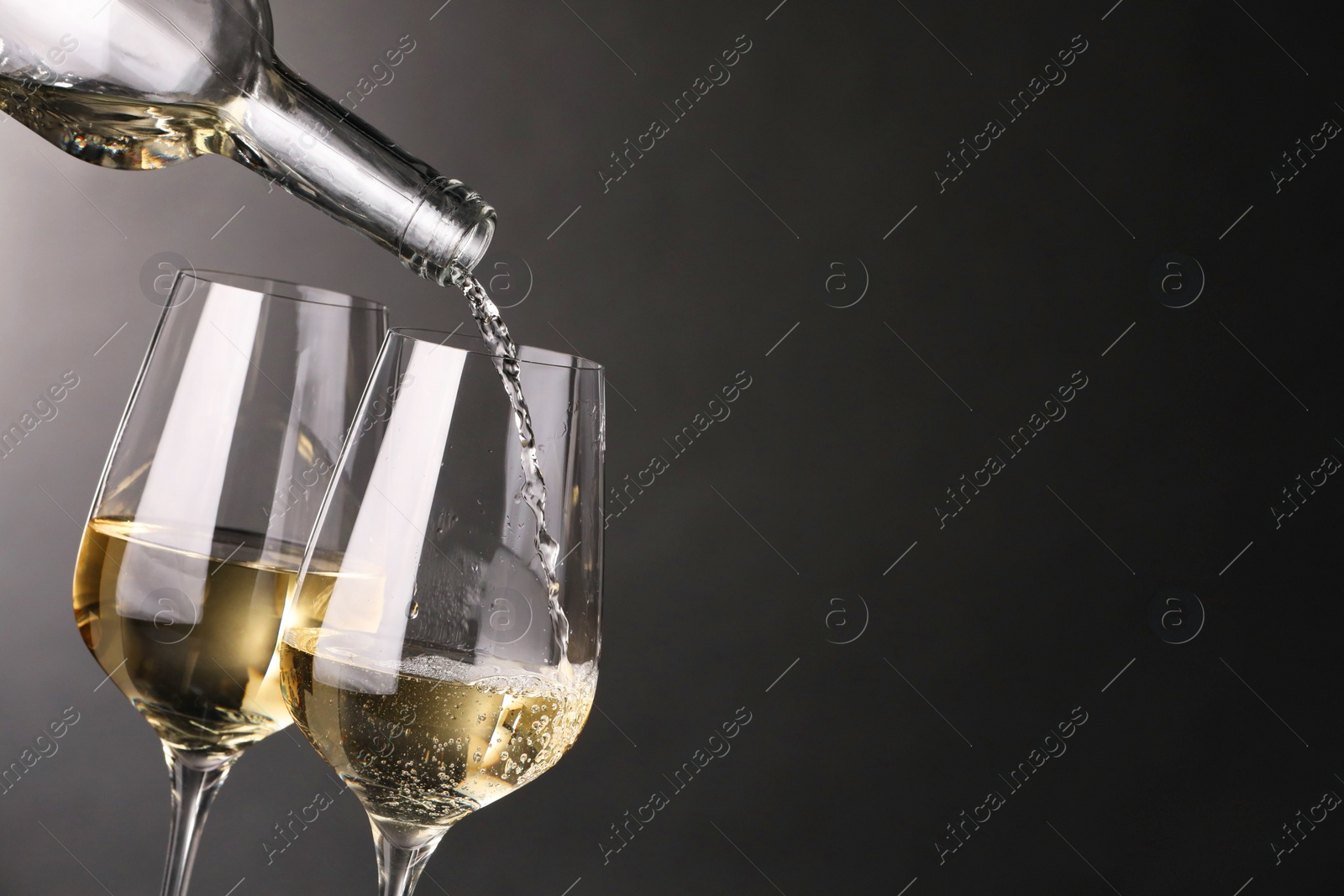 Photo of Pouring white wine into glass against grey background, closeup. Space for text