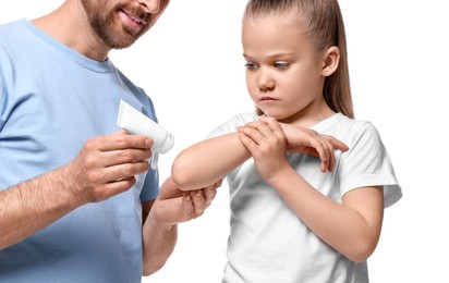 Photo of Father applying ointment onto his daughter's elbow on white background