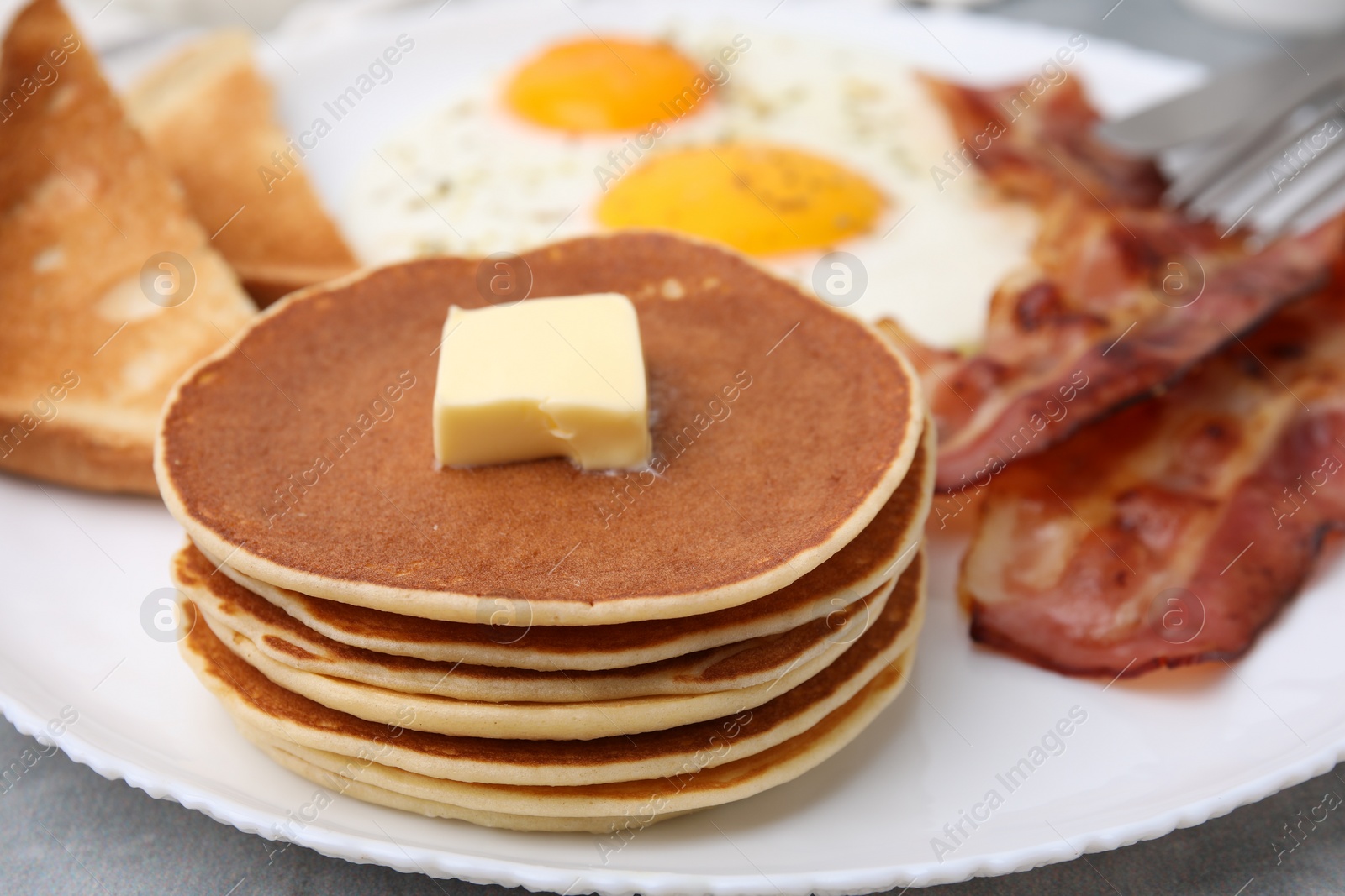 Photo of Tasty pancakes served with fried eggs and bacon on grey table, closeup