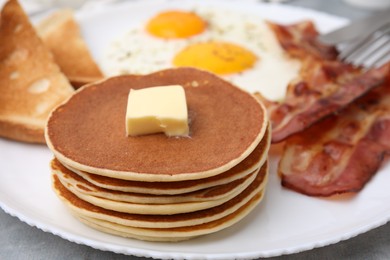 Photo of Tasty pancakes served with fried eggs and bacon on grey table, closeup