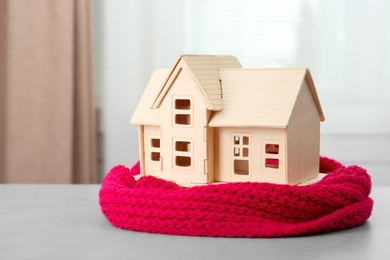 Photo of Wooden house model and scarf on grey table indoors. Heating efficiency