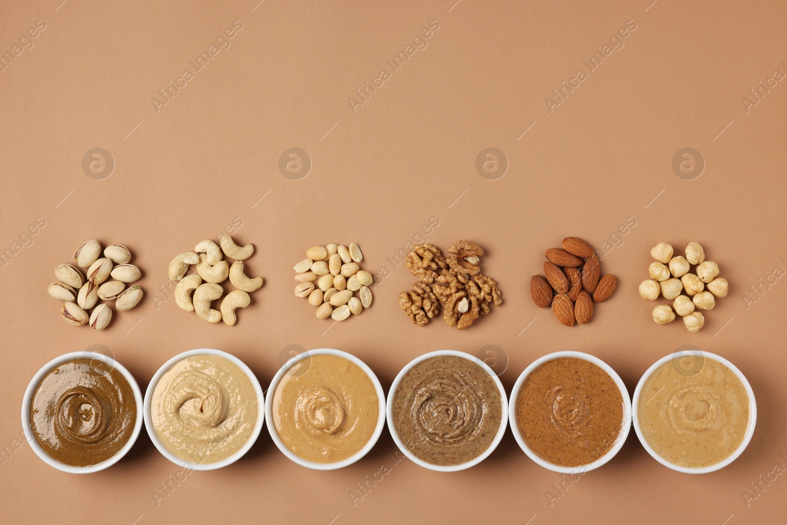 Photo of Many tasty nut butters in bowls and nuts on beige table, flat lay. Space for text