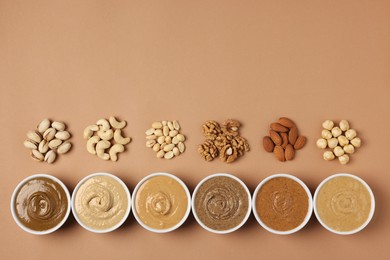 Many tasty nut butters in bowls and nuts on beige table, flat lay. Space for text