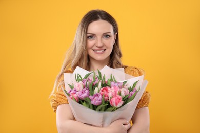 Photo of Happy young woman with bouquet of beautiful tulips on yellow background