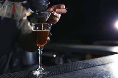 Photo of Barman pouring martini espresso cocktail into glass at counter, closeup. Space for text