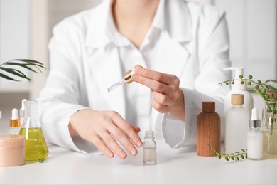 Photo of Dermatologist testing essential oil at white table indoors, closeup