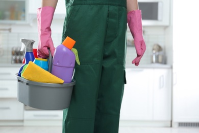 Photo of Worker in uniform with basin of detergents in kitchen, closeup. Cleaning service