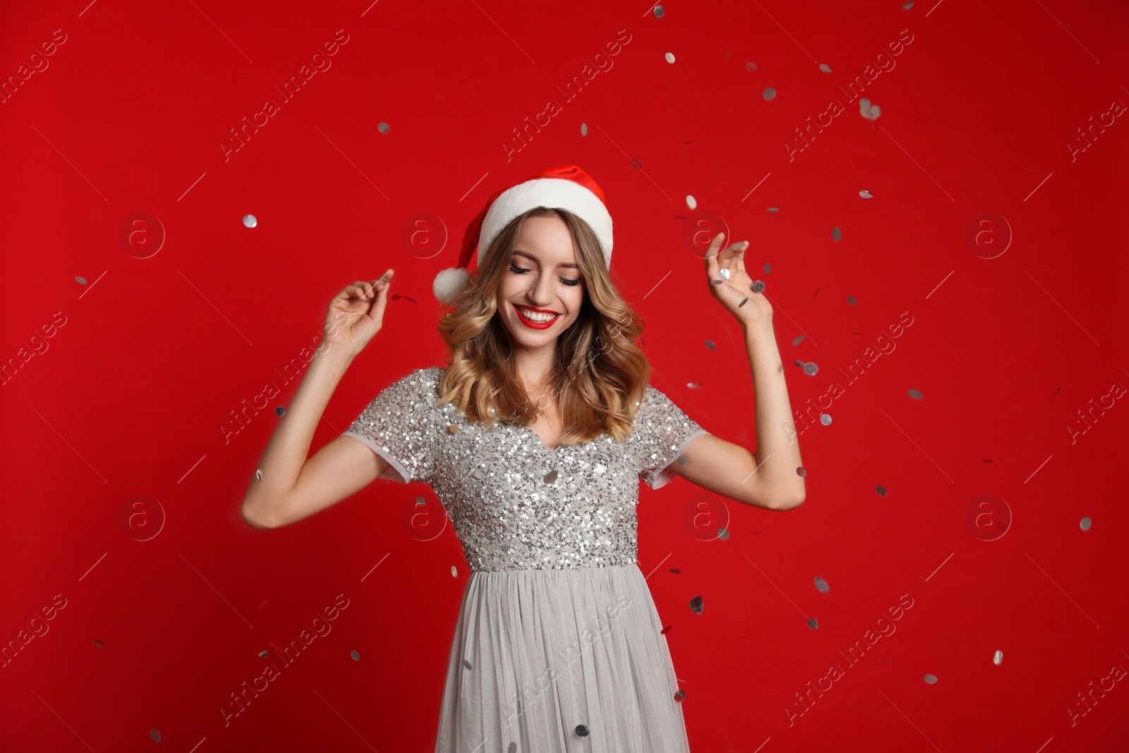 Photo of Happy young woman wearing Santa hat and confetti on red background. Christmas celebration