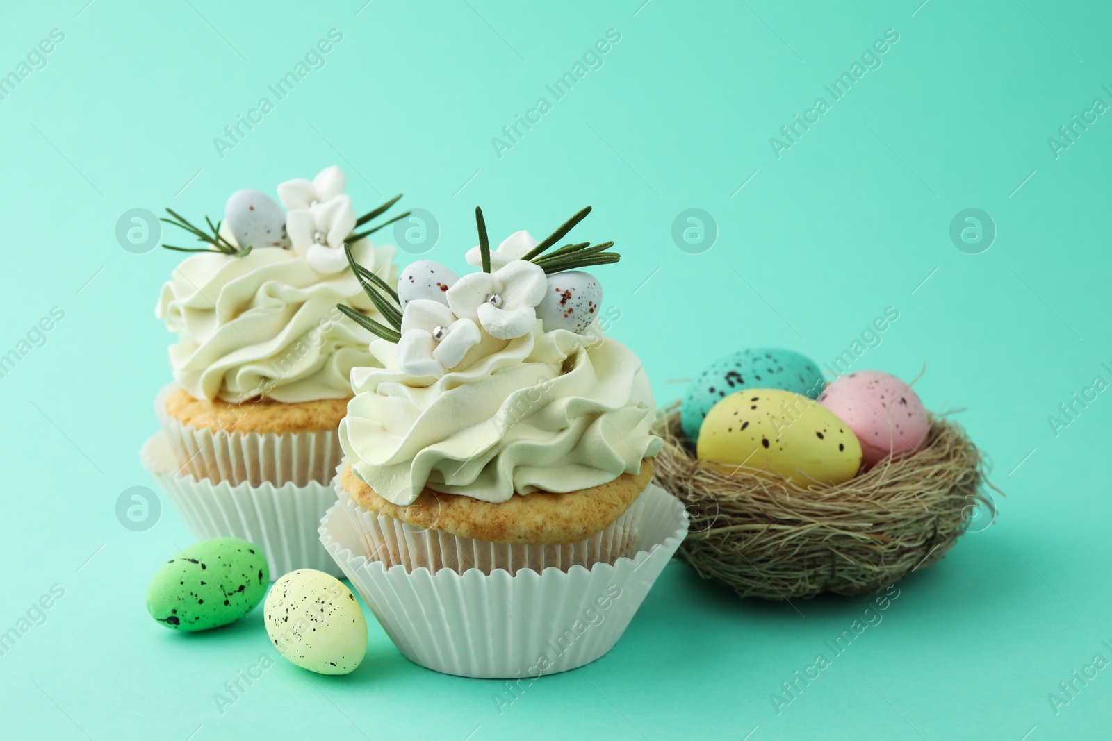 Photo of Tasty Easter cupcakes with vanilla cream and festive decor on turquoise background