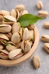 Photo of Delicious pistachios in bowl on grey textured table, closeup