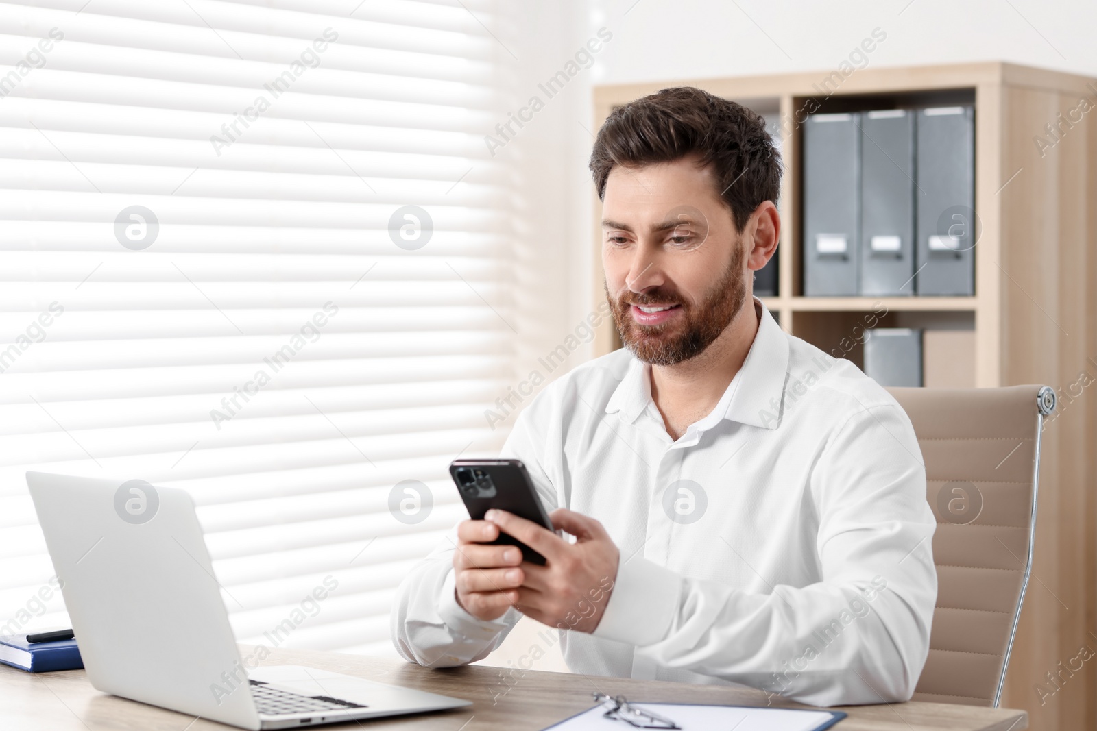 Photo of Smiling man using smartphone at table in office