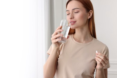 Beautiful young woman with vitamin pill and glass of water. Space for text