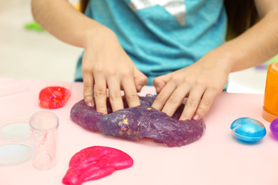 Photo of Girl playing with purple slime at table, closeup