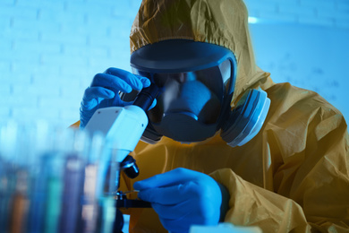 Scientist in chemical protective suit using microscope at laboratory. Virus research