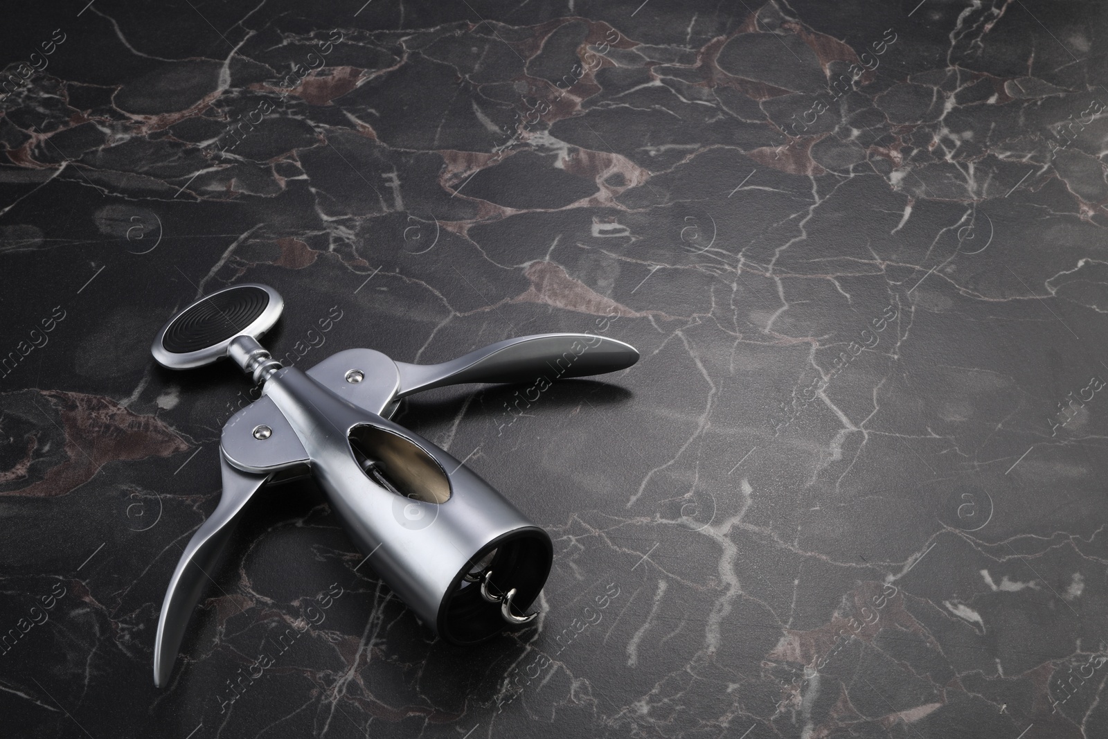 Photo of One wing corkscrew on black marble table. Space for text