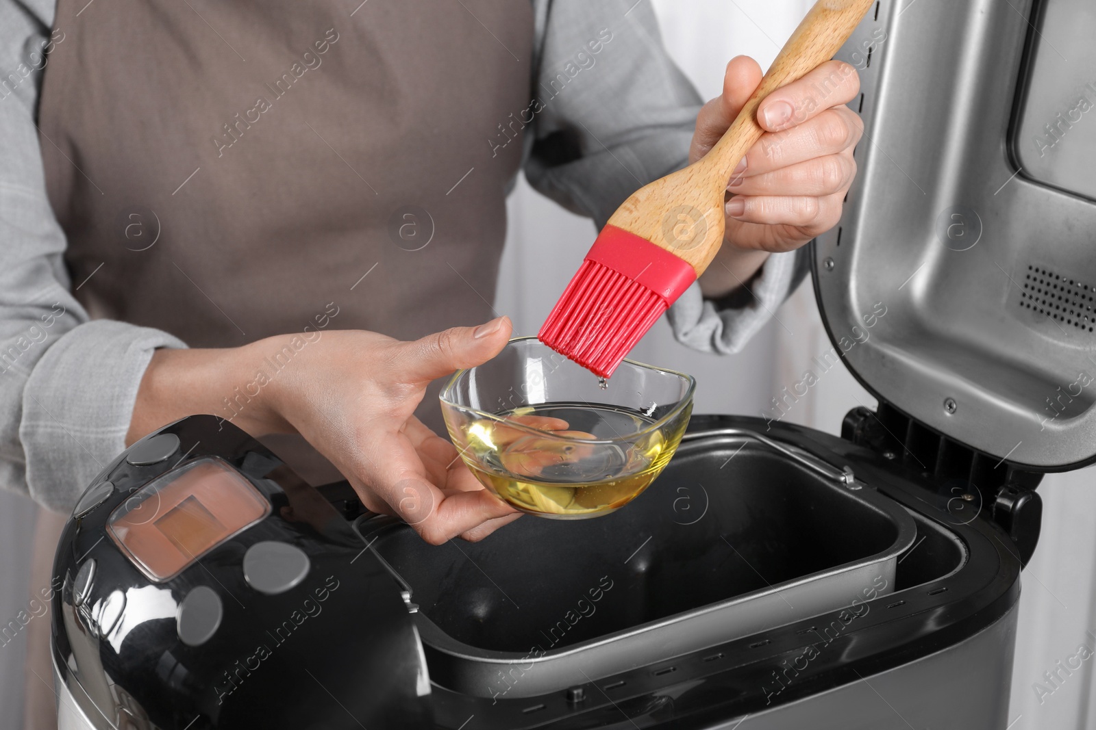 Photo of Woman with oil above breadmaker indoors, closeup