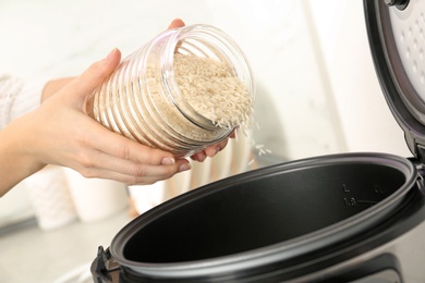 Photo of Woman pouring rice from jar into cooker in kitchen, closeup