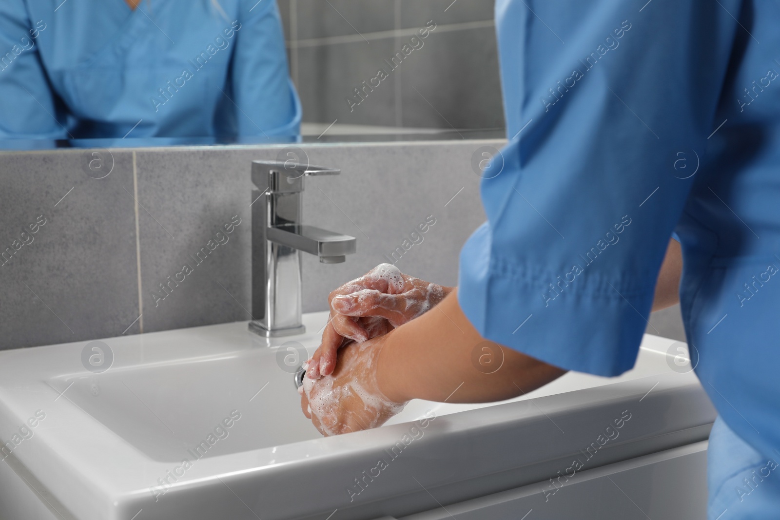 Photo of Doctor washing hands with water from tap in bathroom, closeup