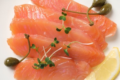 Photo of Delicious salmon carpaccio with capers, microgreens and lemon on white background, top view