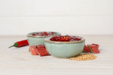 Tasty rhubarb sauce and ingredients on white wooden table, closeup. Space for text