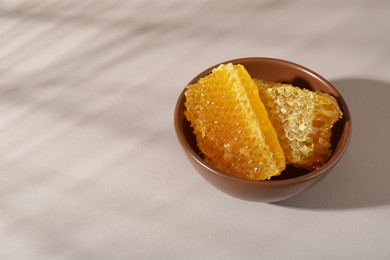 Natural honeycombs in bowl on white table, space for text