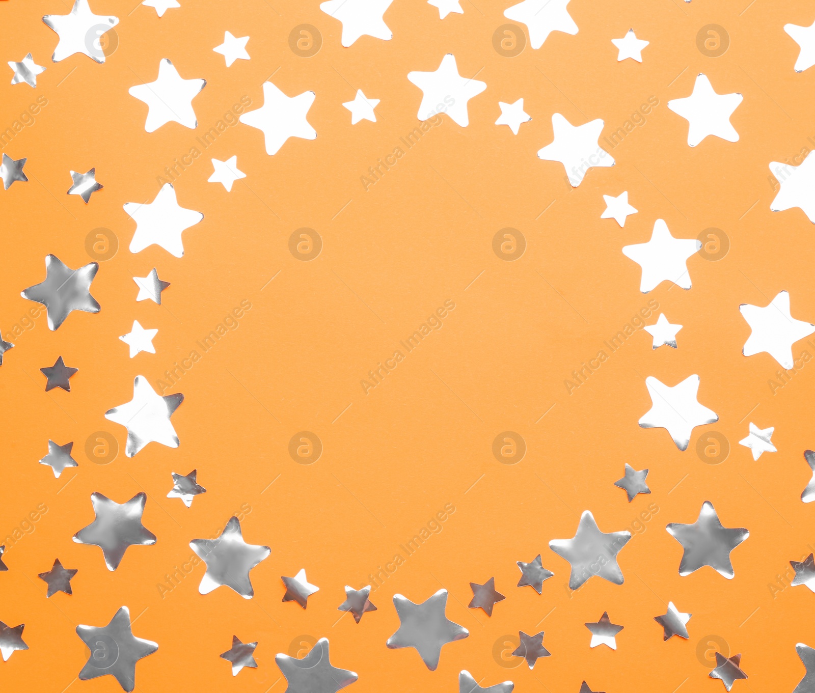 Photo of Frame made of confetti stars with space for text on orange background, top view. Christmas celebration