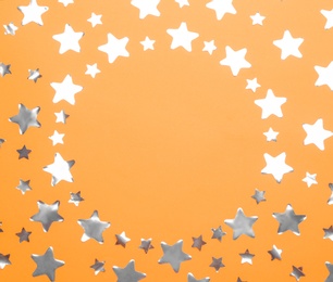 Frame made of confetti stars with space for text on orange background, top view. Christmas celebration