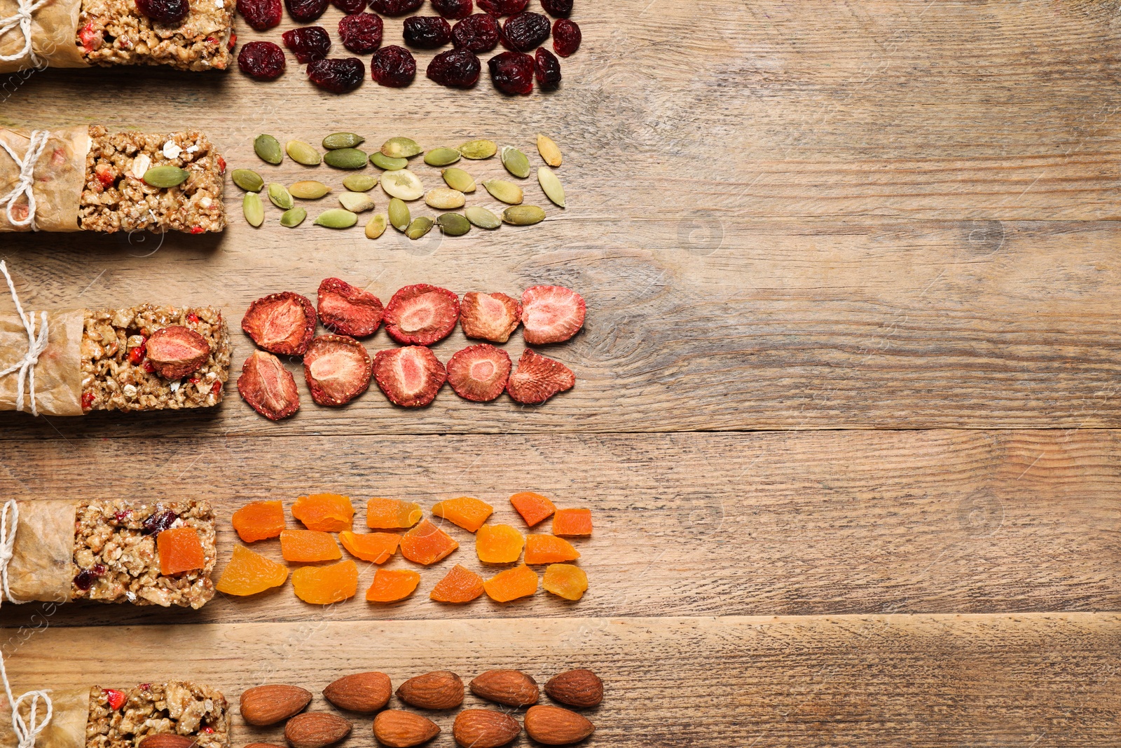 Photo of Different tasty granola bars and ingredients on wooden table, flat lay. Space for text