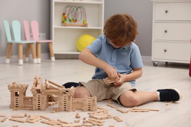 Photo of Little boy playing with wooden construction set on floor in room. Child's toy