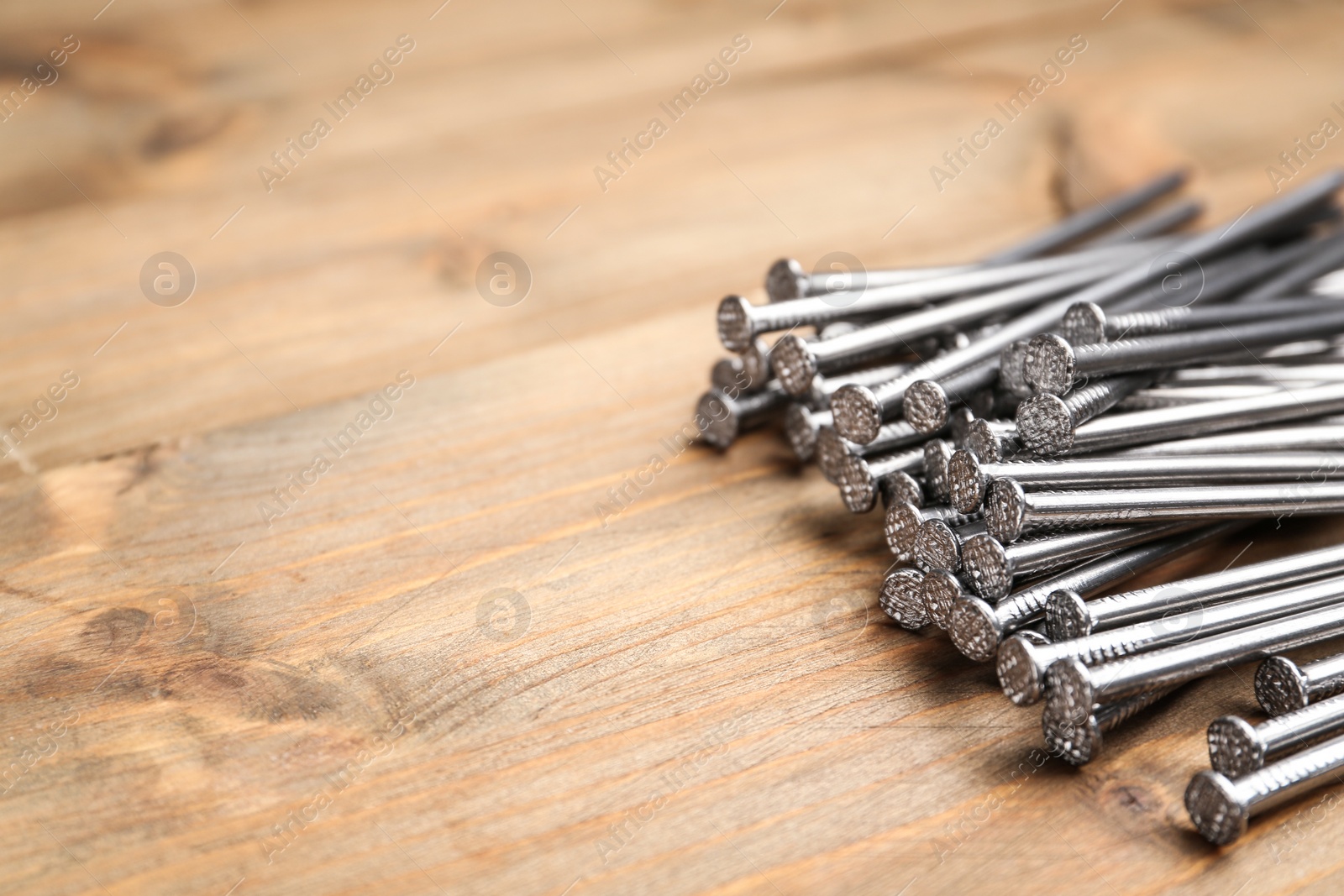 Photo of Pile of metal nails on wooden background, closeup. Space for text