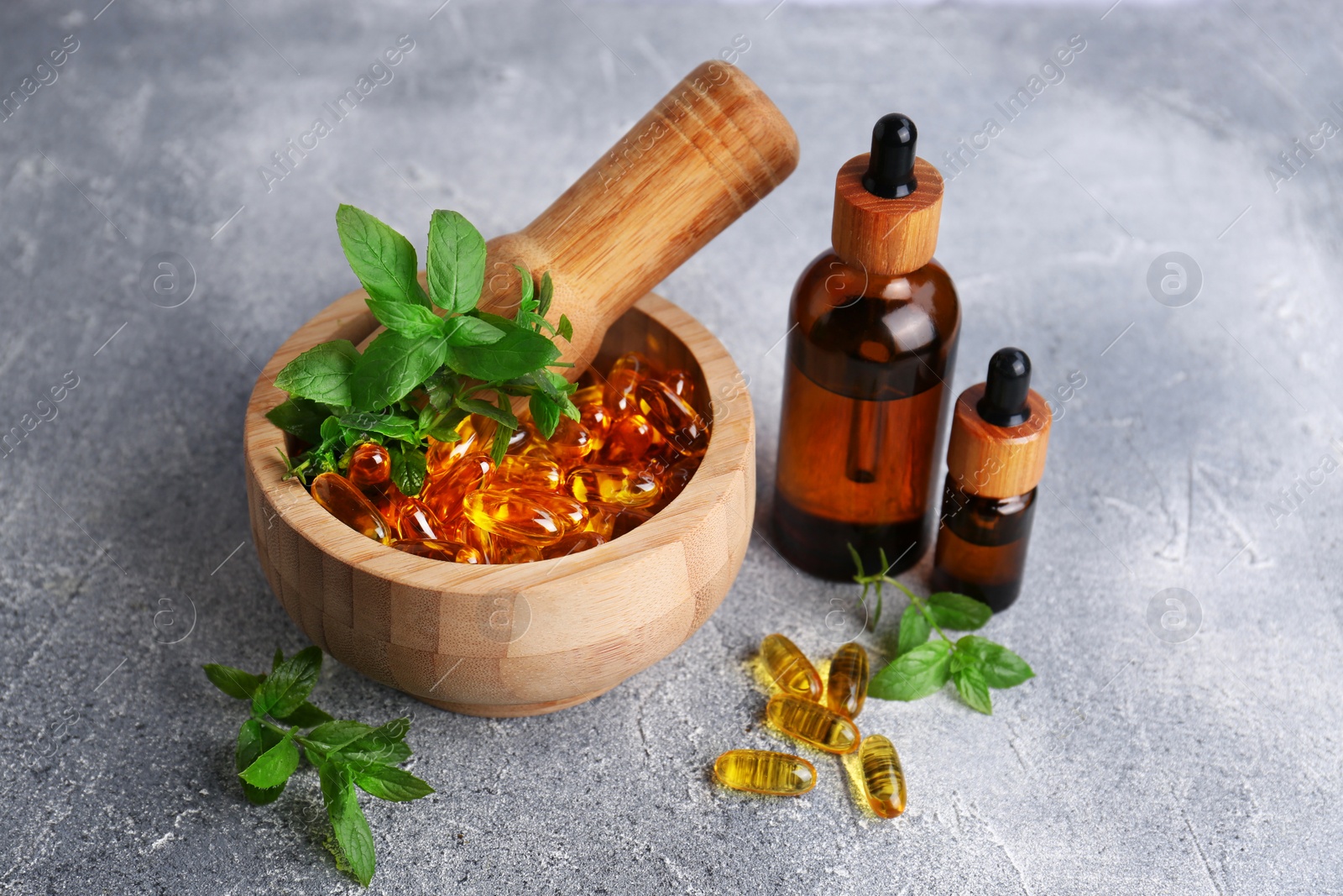 Photo of Wooden mortar with fresh green herbs, extracts and capsules on light grey table