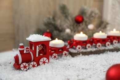Photo of Red toy train as Christmas candle holder on table with artificial snow in room