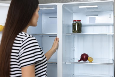 Photo of Young woman near empty refrigerator indoors, selective focus