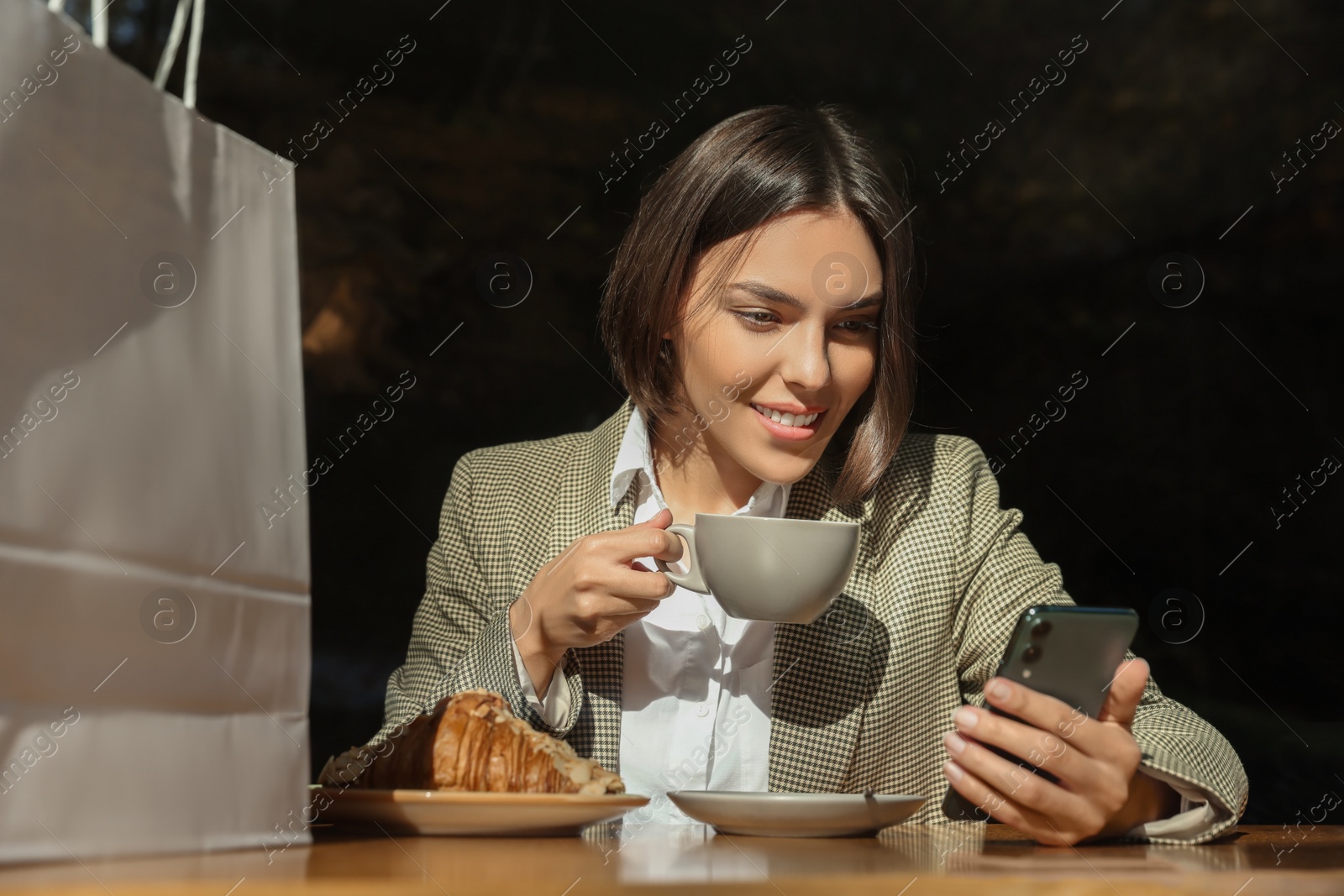 Photo of Special Promotion. Happy young woman with cup of drink using smartphone at table in cafe